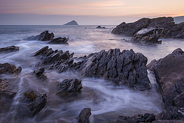 Pastel sunset sky over the Great Mewstone from the rocky shores of Wembury Bay, Devon, England, United Kingdom, Europe