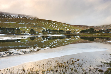 Sunset reflected in the icy waters of the Upper Neuadd Reservoir, with Graig Fan Ddu escarpment in the background in winter, Brecon Beacons National Park, Powys, Wales, United Kingdom, Europe