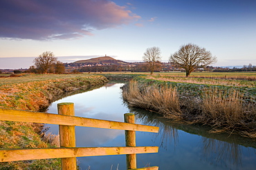 First light of a winter morning on Glastonbury Tor viewed from the River Brue on the Somerset Levels, Glastonbury, Somerset, England, United Kingdom, Europe