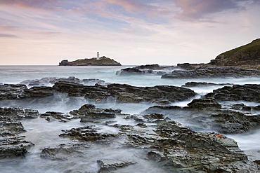 Waves crash over the rocks of Godrevy Point at sunset, looking towards Godrevy Lighthouse, Cornwall, England, United Kingdom, Europe