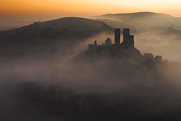 A sea of mist swirls around the base of Corfe Castle at dawn, Corfe, Dorset, England, United Kingdom, Europe