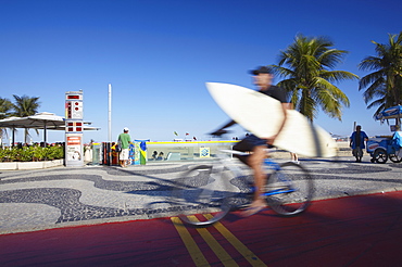 Man with surfboard cycling along Avenida Atlantica, Copacabana, Rio de Janeiro, Brazil, South America 