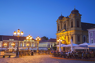 Roman Catholic Cathedral and outdoor cafes in Piata Unirii at dusk, Timisoara, Banat, Romania, Europe 