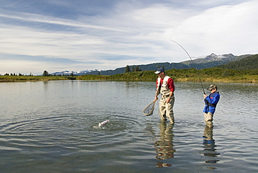 Boy catching a Silver (Coho) salmon (Oncorhynchus kisutch) with dad's help, Coghill Lake, Alaska, United States of America, North America