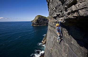 A climber hangs above the sea on the huge west face of Dun Mingulay cliff, Mingulay Island, Outer Hebrides, Scotland, United Kingdom, Europe