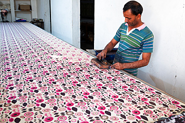 Man using carved and inked wooden blocks to block print large bolt of cotton fabric before rinsing then leaving in the sun to dry.