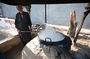 Street dahi (curd) maker stirring the dahi in a metal bowl over a clay covered oven