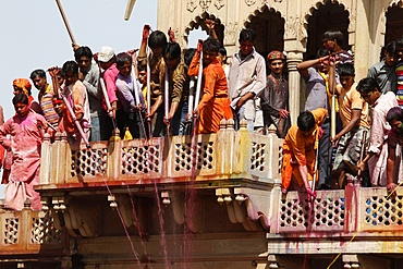 Young men celebrating Holi festival by splashing colored fluids on temple visitors, Nandgaon, Uttar Pradesh, India, Asia