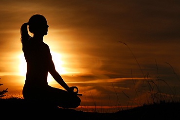 Silhouette of a woman in lotus position, practising yoga against the light of the evening sun, French Alps, France, Europe