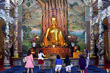 Sitting golden Buddha figure in main hall and worshippers praying to the Buddha, Linh Phuoc Pagoda, Dalat, Vietnam, Indochina, Southeast Asia, Asia