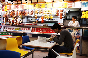 Man in cafe with hanging roast duck and pork and Chinese menus, Hong Kong, China, Asia