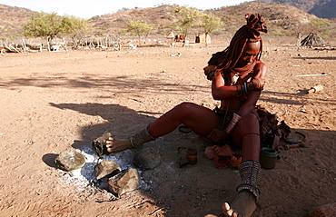 A young Himba woman covering her body with a mix of clay and resin for protection against the sun and insects, and as body decoration, near the Kunene River, Namibia, Africa 