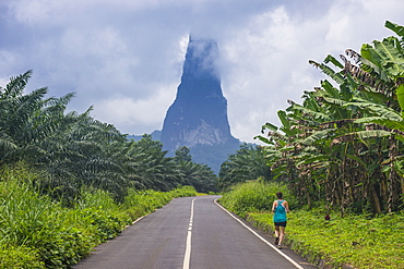 Runner on a road leading to the unusal monolith, Pico Cao Grande, east coast of Sao Tome, Sao Tome and Principe, Atlantic Ocean, Africa