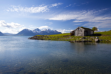 Cabin with traditional grass roof overlooking a fjord and snowy mountains in Lyngen Peninsula, Troms county, Norway, Scandinavia, Europe