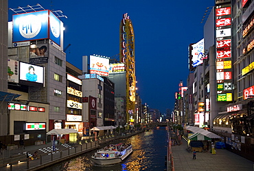 Tour boat on Dotonbori River glides past shops and restaurants in Namba, Osaka, Japan, Asia