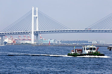 Tug boat passing by the Yokohama Bay Bridge which spans the Tokyo Bay in Yokohama, Japan, Asia