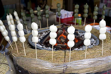 Japanese snack called dango (three sticky rice cake balls on a skewer) warming beside hot coals, Japan, Asia