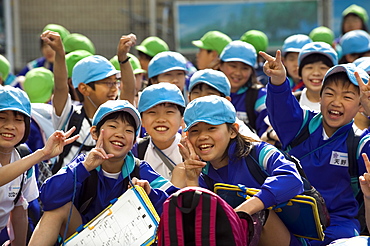 Group of smiling Japanese elementary school children wearing blue and green caps, Japan, Asia