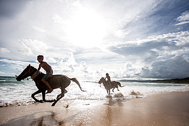 Two young boys and their horses play in the ocean in Nihiwatu, Sumba, Indonesia, Southeast Asia, Asia