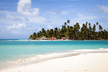 Palm trees and thatch huts on Diablo Island seen from the beach on Dog Island, San Blas Islands, Panama, Central America