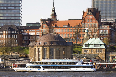 A tour boat docks by the St. Pauli Landing Stages (Landungsbruecken) while buildings of St. Pauli overlook the harbour in Hamburg, Germany, Europe