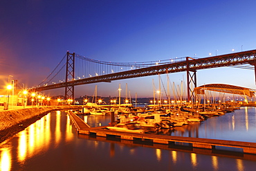 Boats on the River Tagus move at night in the Doca de Santa Amaro marina under the 25 April Bridge, Lisbon, Portugal, Europe