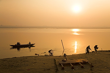 People go about their daily business as the sun rises over the Ganga (Ganges) River at Varanasi, Uttar Pradesh, India, Asia