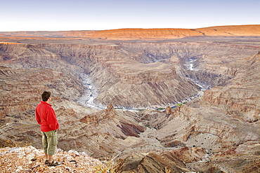 A man stands looking out across the Fish River Canyon in southern Namibia at dawn, Namibia, Africa