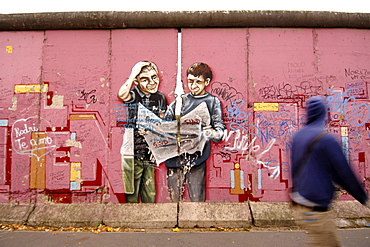 A man walks past a colourful pink mural at the East Side Gallery, a preserved section of the Berlin Wall, Berlin, Germany, Europe