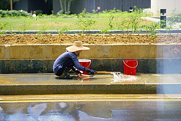 An elderly woman in a straw hat washes the pavement of Raffles Place in the financial district of Singapore, Southeast Asia, Asia