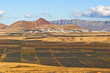 View across black volcanic cinder fields to the town of Soo and the Risco de Famara range with the highest point on the island at Penas del Cache radar site, Soo, Lanzarote, Canary Islands, Spain, Atlantic Ocean, Europe