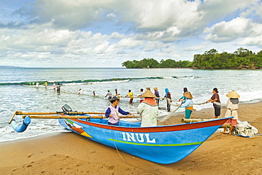 Outrigger fishing boat and people pulling net in by hand to shore near Batu Karas, Pangandaran, West Java, Java, Indonesia, Southeast Asia, Asia