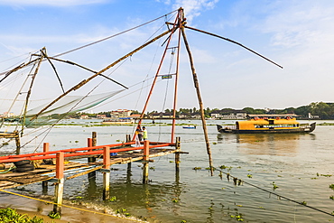 Old Chinese fishing nets and tour boat on the waterfront of Vypin Island with Fort Cochin beyond, Fort Vypin, Kochi, Kerala, India, Asia