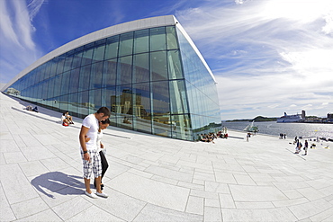 Young couple walking outside the Oslo Opera house exterior in summer sunshine, city centre, Oslo, Norway, Scandinavia, Europe