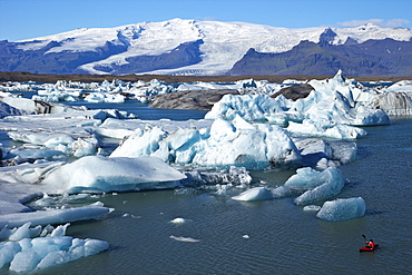 Canoeist paddles between icebergs on glacial lake at Jokulsarlon with snow on the massive icecap of Vatnajokull behind, Iceland, Polar Regions