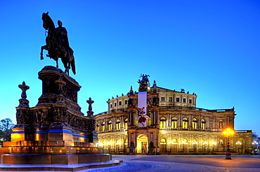 Night scene, illuminated Semperoper opera house with flags and Koenig-Johann-Denkmal monument on the Theaterplatz square, Dresden, Saxony, Germany, Europe