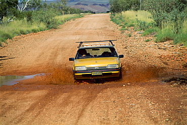 Car driving through a puddle on a red dirt road, Western Australia, Australia