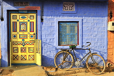 Front door decorated with ornaments and a bicycle in front of a blue wall in an Indian village, Thar Desert, Rajasthan, India, Asia