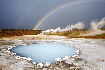 Blahver, blue spring, the most beautiful blue water pool in Hveravellir in the Highlands, in front of Oeskjuholt, a steaming calc-sinter mound which looks like a mini volcano, below a rainbow, Hveravellir, Iceland, Europe