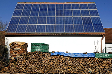 Photovoltaic system on the tool shed of a farm, with firewood stacked in the front, Kalchreuth, Middle Franconia, Bavaria, Germany, Europe