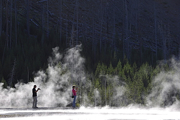 Tourists taking photos while on a boardwalk amidst the steam of the springs and geysers, Black Sand Basin, Upper Geyser Basin, Yellowstone National Park, Wyoming, United States of America, USA