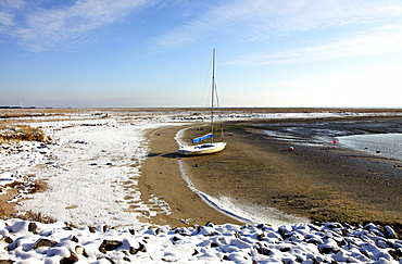 Bay in the Wadden Sea with a sailing boat, snow-covered beach on the East Frisian North Sea island of Spiekeroog, Lower Saxony, Germany, Europe