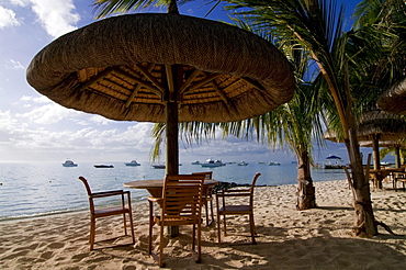 Table and chairs under sunshade on the beach of Le Paradis Hotel, Mauritius, Africa