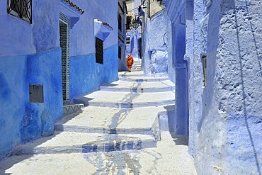 A woman walking in an alleyway painted blue in the medina of Chefchaouen, Morocco, Africa