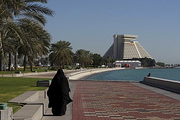 Arabian woman wearing traditional black clothing going for a walk along the Corniche in front of the Sheraton Hotel, West Bay District, Doha, Qatar, Middle East