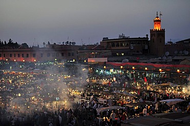 Evening at the Djemaa el Fna market square, literally meaning Assembly of the Dead, with smoke from the many food stalls, behind, the minaret of a mosque, Marrakech, Morocco, Africa