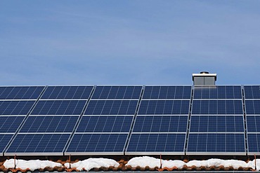 Solar panels on the roof of a house with patches of snow, renewable energy