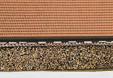 Large covered wood pile in winter, above it a red tile roof, wood industry