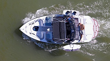 Man taking a sunbath on the deck of a moving sports boat, equipped with wakeboards, from above