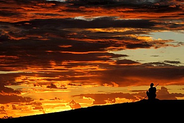 Australian Aboriginal sitting on a hill looking into sunset sky, Northwest Australia